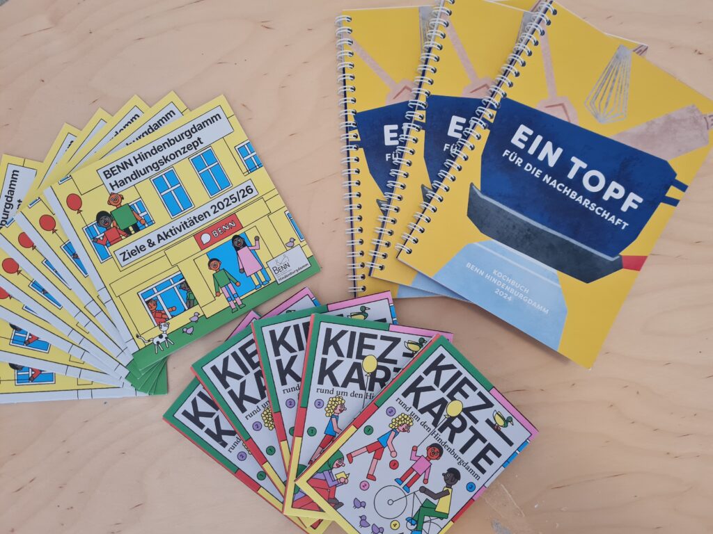 Auf einem Tisch liegen die Kiezkarte, das Handlungskonzept und das Kochbuch.