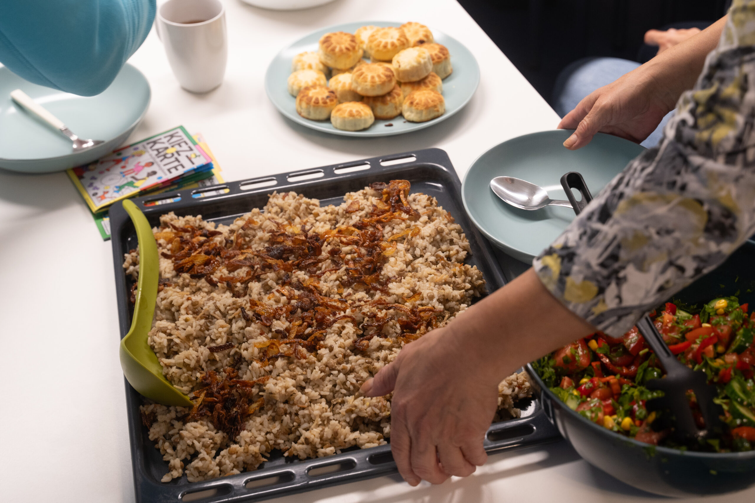 Auf einem Tisch steht ein Bleck mit Reis, Linsen und Zwiebeln.