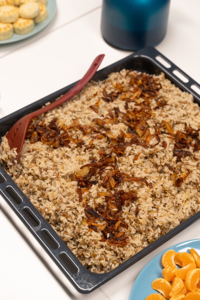 Auf einem Bleck sind Reis und Linsen, mit gerösteten Zwiebeln bestreut.