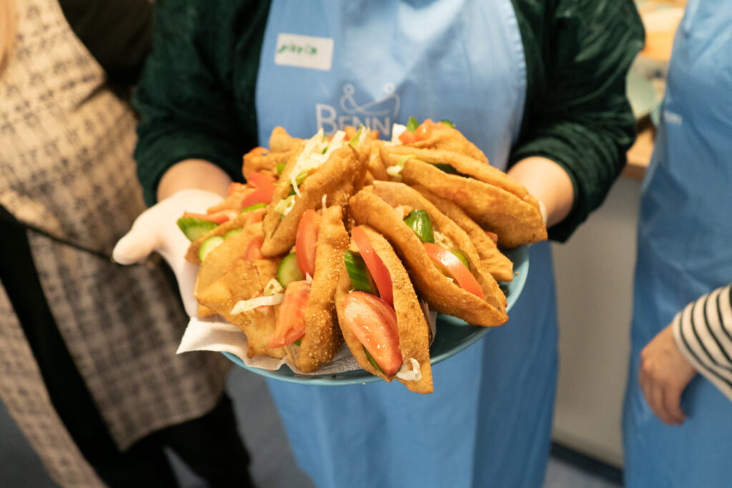 Eine Frau mit Schürze hält einen Teller voll mit kleinen Sandwiches.