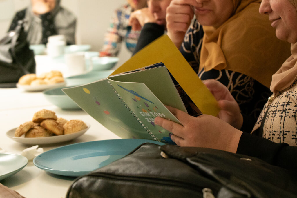 Viele Frauen sitzen an einem Tisch und lesen in dem Kochbuch.