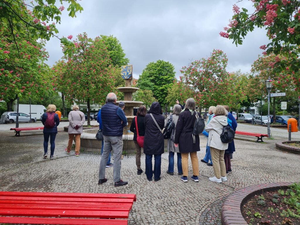 Vor einem Brunnen steht eine Gruppe Menschen.